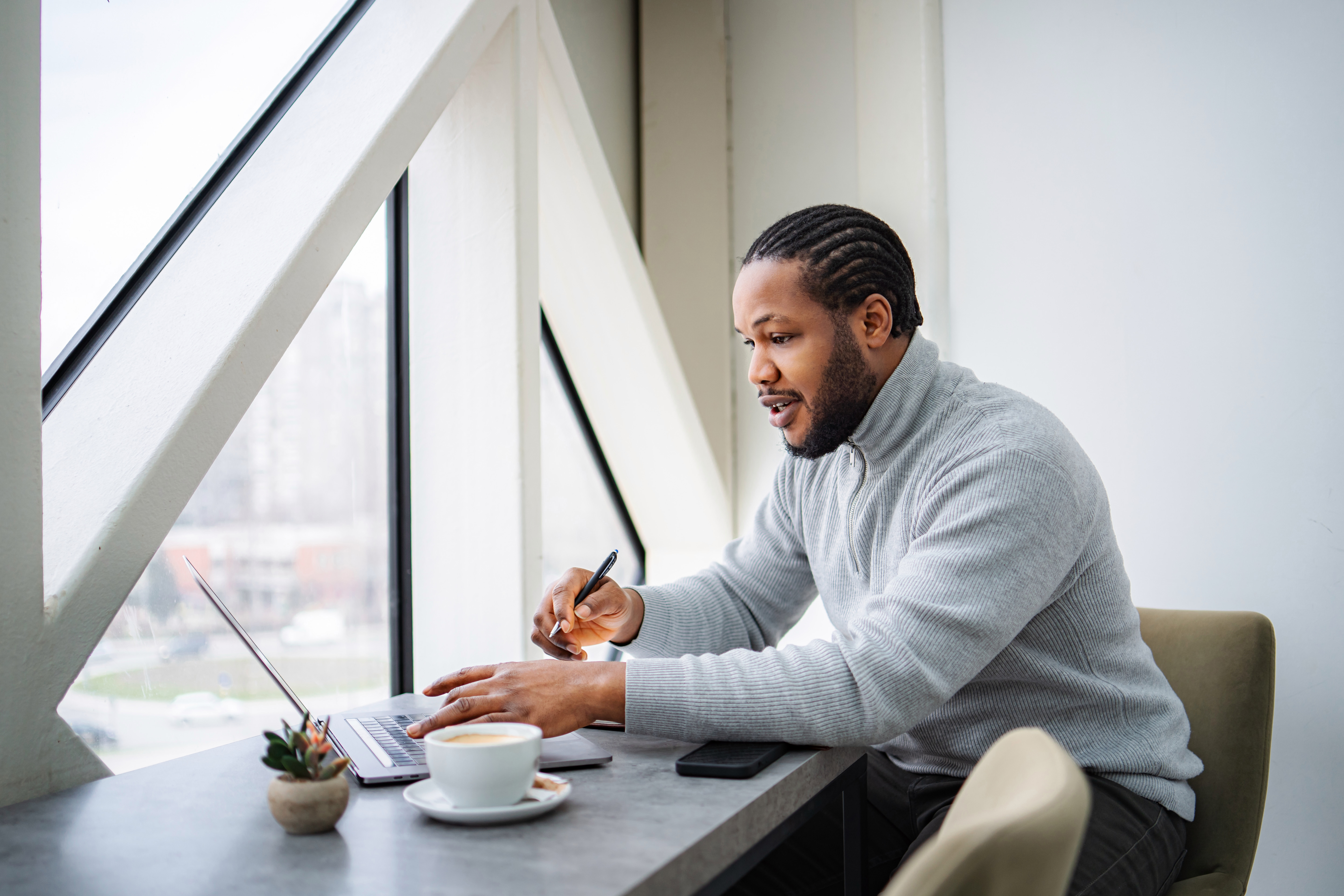 Man focusing on his laptop, working remotely in a bright modern cafe